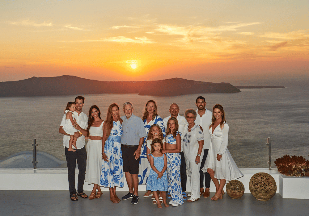 A family poses for a sunset photo on a balcony at Erossea Villa Santorini, with a stunning ocean view in the background