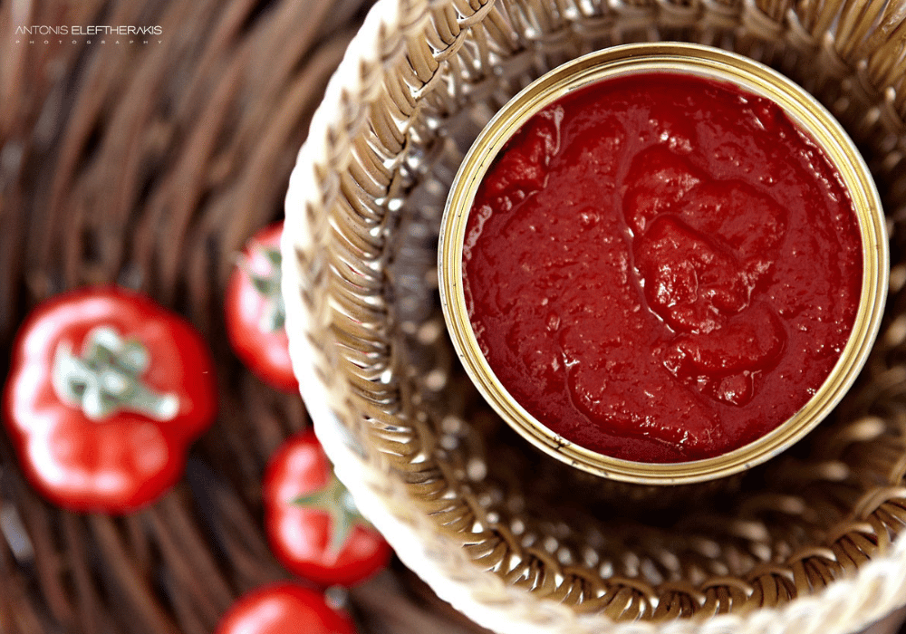 A basket filled with ripe tomatoes and a can of tomato sauce, representing Erossea Villa Santorini's private chef services