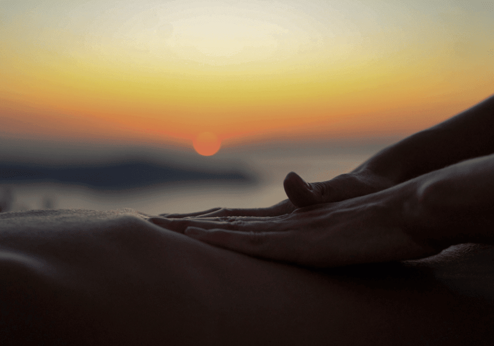 A serene sunset scene featuring a person receiving a massage at Erossea Villa Santorini, embodying relaxation and tranquility