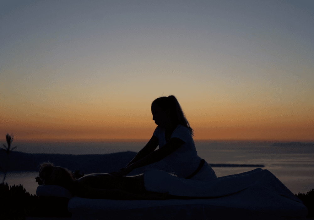 A woman enjoys a relaxing massage at sunset at Erossea Villa, Santorini, surrounded by serene beauty and tranquility