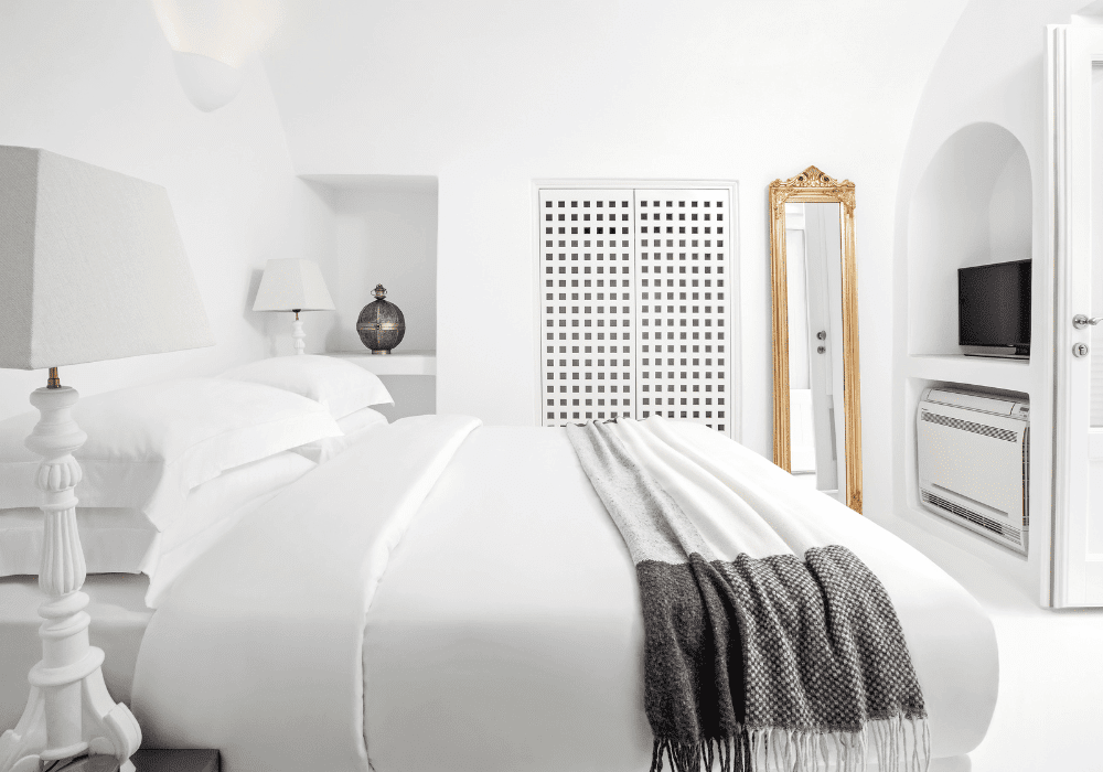  Tranquil white bedroom in Erossea Villa Santorini, complete with a bed, mirror, and television for a cozy atmosphere