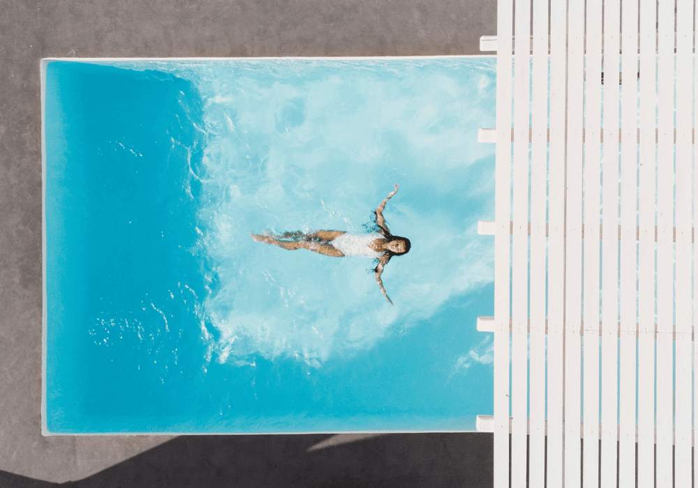 A woman gracefully floats in a serene pool at Erossea Villa Santorini, framed by a charming white pergola