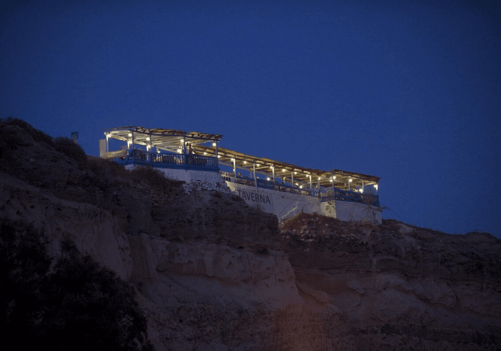 A taverna perched on a cliff at night, illuminated against the dark sky, showcasing Santorini Fresh Seafood at Vlychada Marina